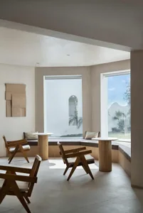A modern lounge area with concrete walls, wooden furniture, and large windows.