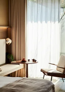 A modern minimalist bedroom featuring textured fabric upholstery, a small round table with a teapot and apples, and natural l