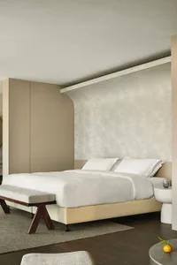 A modern minimalist bedroom featuring a white bed with white bedding.