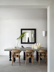A modern minimalist dining room featuring a concrete table and wooden chairs, with a large mirror on the wall, candles, and a