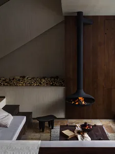 A modern minimalist living room with a wood fireplace, a grey couch, and a coffee table with a bowl of fruit and a book on a 