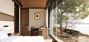 A modern, minimalist bedroom featuring wooden furniture and large glass windows with a scenic lake view.
