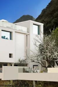 A modern residential building with a minimalist design, featuring concrete and glass materials, set against a mountainous bac