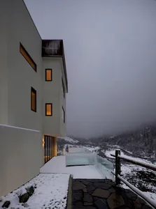 Modern residential building with white exterior and snow-covered roof and landscape.