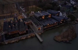 A modern residential space featuring glass roofs and gray-tiled facades surrounded by a water body, with a parking area and t