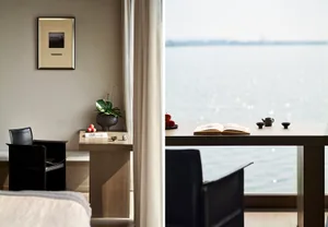 A modern residential space featuring a wooden table with fruit and books, overlooking a serene water vista.
