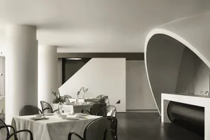 Interior of a modern restaurant with concrete walls and floors, white tables and chairs, and minimalist design.
