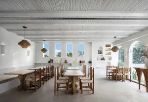 A minimalist restaurant interior featuring white concrete walls, wooden tables and chairs, and concrete floors.