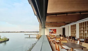 Modern restaurant interior with glass walls overlooking a serene waterfront.