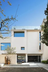 A modern residential house with white rendered concrete exterior and large glass windows.