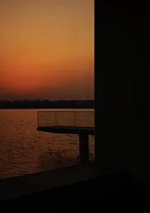 玻璃欄杆俯瞰寧靜湖面上的夕陽，前景為水磨石平台。