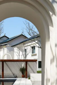 A white plaster residential space with a wooden pergola and potted plants under an archway.
