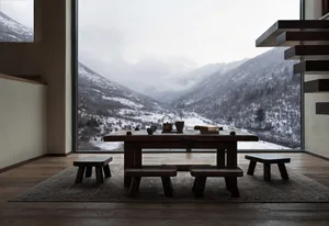 Minimalist interior design featuring a wooden table and stools with a scenic mountain view through large windows.