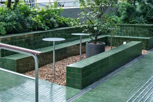 A landscaped area with green tiled benches, planters, and a few trees.