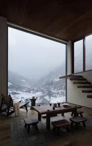 A minimalist living room with a large window showcasing a mountainous landscape, featuring wooden furniture and floor-to-ceil