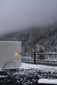 A minimalist white structure surrounded by a snowy landscape with a wooden fence.