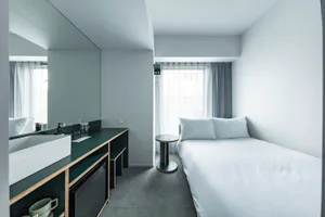 A modern minimalist bedroom with a white cushion and bed against a white wall and floor.