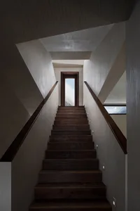 Modern, wooden staircase with industrial design elements, featuring a hallway with a door opening towards a sky view.