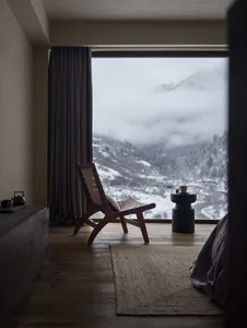 A bedroom with a mountain view, featuring a wooden chair and a side table with a cup and saucer.