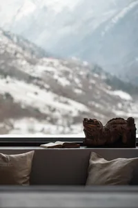A cozy living room with a carved wooden lion statue, a book, and cushions overlooking a snowy mountain landscape.