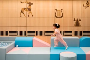 A child in a pink outfit running on soft play structures in a modern playroom