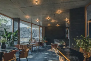 Interior design of an industrial cafe with concrete walls and floor, featuring wooden tables and chairs, and natural lighting