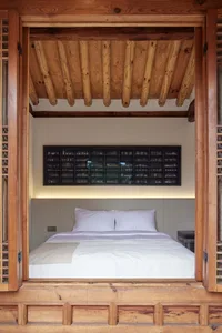 A minimalist bedroom with a bed nestled within a wooden box, featuring a display case filled with ceramics on the wall.
