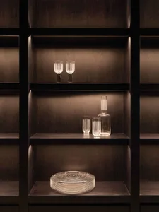 A minimalist interior design featuring glass objects on dark wooden shelves with warm lighting.