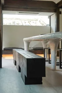 A minimalist interior with a wooden bench and a metal curved table.