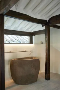 A minimalist bathroom interior featuring a stone tub and a window with a view of tiled rooftops.