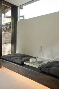 A minimalist living space featuring a wooden window seat with pillows and a glass tray with decorative items placed on top of