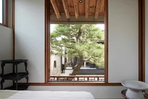 A minimalist window view of a traditional wooden house, showing a tree and a serene outdoor space.