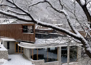 Modern architectural exterior of a building covered in snow, featuring wooden accents and large glass windows.