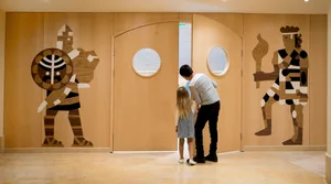 A modern entrance decorated with wood, featuring two wooden human-like figures.