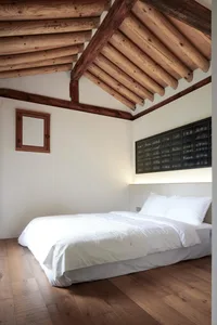 Modern minimalist bedroom with wood furnishings, white bedding, and a wooden ceiling with exposed beams.