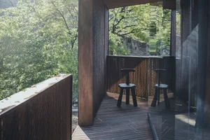A modern outdoor wooden balcony with greenery in the background.