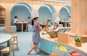 Children playing in a modern, brightly lit playroom with wooden furniture and natural materials.