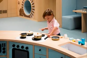 A child plays in a toy kitchen, engaging with a toy stove and pots and pans.