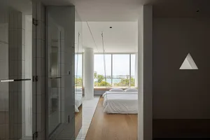 Bedroom with white tiled walls and hardwood floors, featuring a white bed with white bedding, large windows overlooking the s