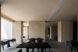 A minimalistic restaurant interior featuring concrete walls and metal tables and chairs.