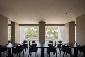 A modern cafe with wooden tables and chairs, large windows overlooking a garden.