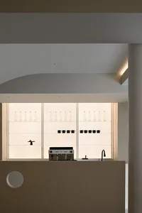 A minimalist coffee bar with glass shelves displaying water bottles and coffee mugs.