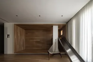 Modern minimalist living room featuring a wooden floor and walls, with a white chair and a metallic slide.