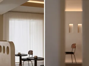 A minimalist coffee shop with neutral-toned lighting, featuring two small round tables and chairs.