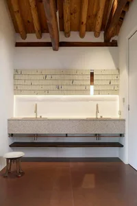 Modern bathroom featuring a granite countertop with two sinks, a wooden ceiling with exposed beams, and under-cabinet lightin