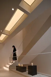 Modern minimalist interior with a focus on a sleek and contemporary staircase with glass railings and warm lighting.