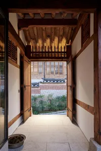 A traditional wooden doorway leading to a stone-paved courtyard, surrounded by traditional Korean architectural elements.