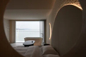 A modern bedroom featuring a concrete floor, glass walls, and minimalist decor.