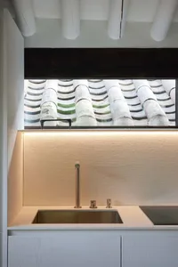 A minimalist residential kitchen featuring a white countertop, metal sink, and textured backsplash.