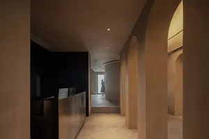 A modern architectural corridor with arched openings and concrete walls, featuring a person standing in the distance.